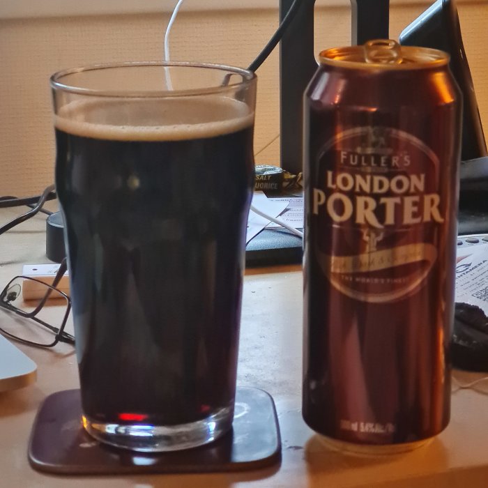 Ett glas mörkt öl bredvid en burk Fuller's London Porter på ett bord.