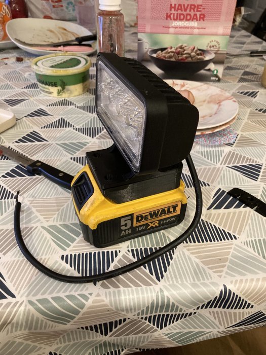 DeWalt arbetslampa på bord med oordning, laddningsbart batteri och byggstart indikeras.