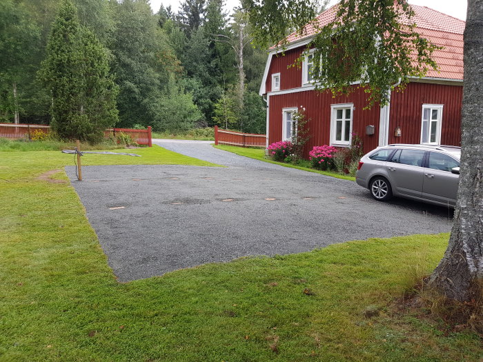 Nyutlagd markduk och grus framför rött hus med grönt gräs och parkerad bil.