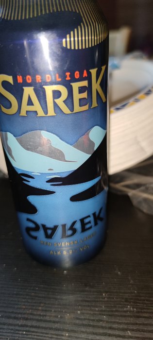 En ölburk märkt "Sarek" med texten "Ren Svensk Lager" och en fjällbild i bakgrunden.