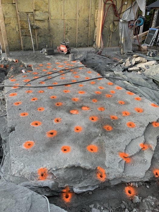 Beton med oranga markerade borrhal for sprangning, omgivande byggutrustning synlig.