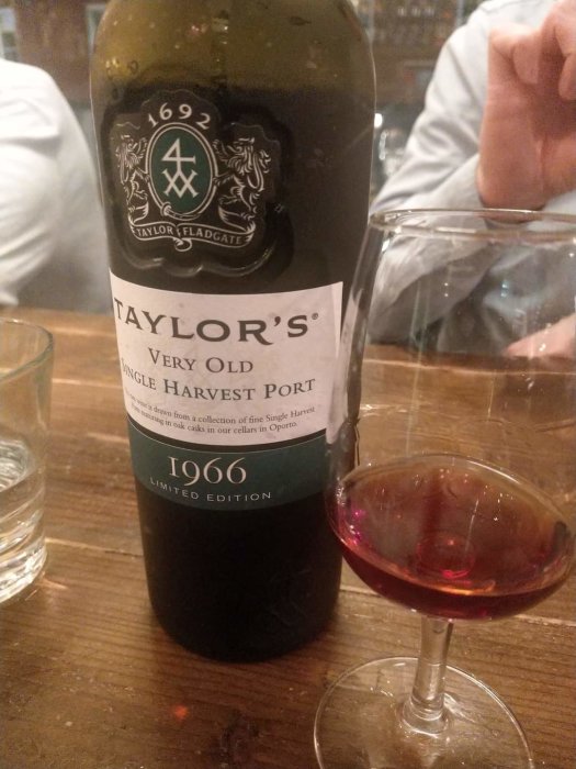 Flaska Taylors Very Old Single Harvest Port 1966 bredvid ett glas med portvin på ett träbord.