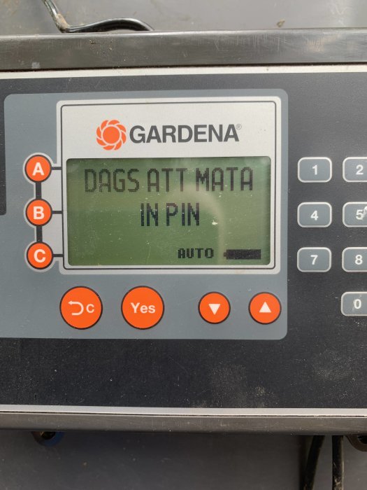 Display på en gräsklippare med texten "DAGS ATT MATA IN PIN" och knappsats intill.