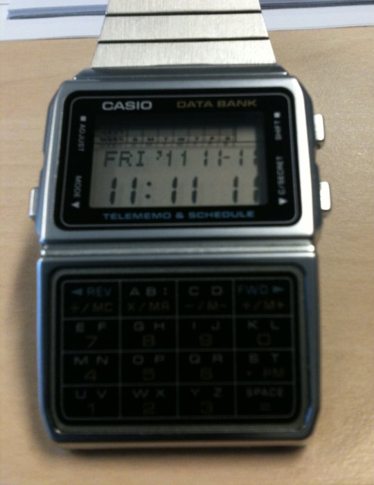 En Casio Data Bank digital klocka på ett bord som visar datum och tid.