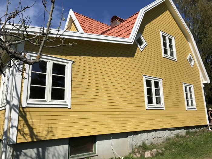 Gulmålat hus med torpargrund och en äldre källare synlig, mot en bakgrund av blå himmel.