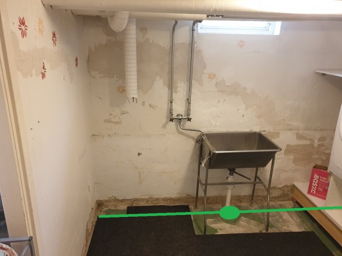 En tvättstuga i källaren med befintliga avloppsrör och gröna linjer som markerar planerade nya avloppsrör.