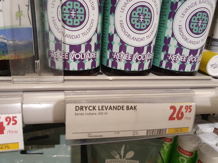 Flaskor av Renée Voltaire Dryck Levande Bak med prisinformation i en butikshylla.