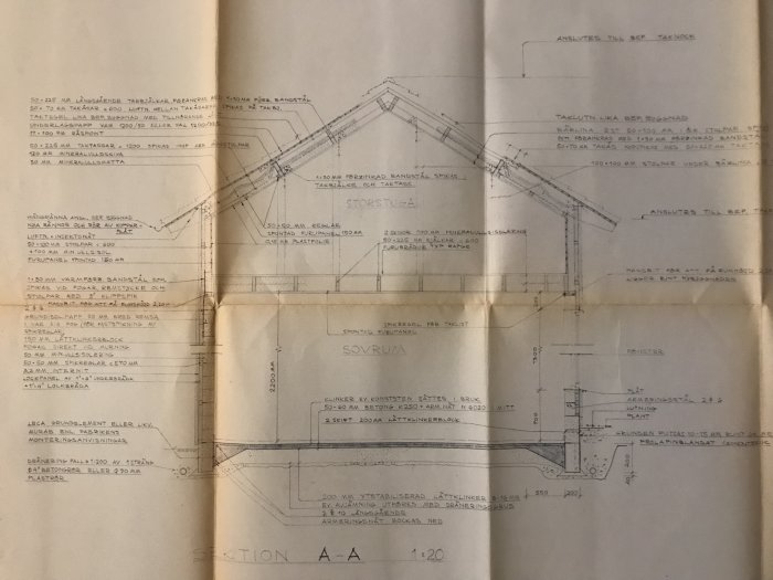 Öppen arkitektritning som visar sektion A-A av en byggnad med markerade vinklar, mått, och en penna på pappret.