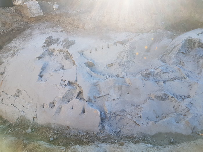 Bergyta med hål efter borrning och sprickbildning, närbild på sprängningsförsök i berg.