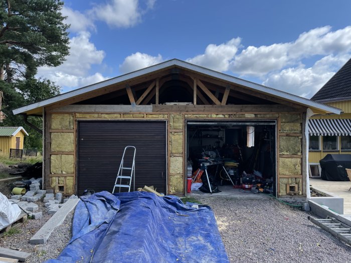 Garage under renovering med avlägsnad panel och synlig W-konstruktion av trä i taket.