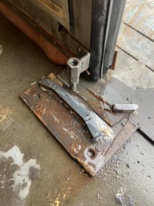 Svetsad metallkonstruktion med synliga svetsfogar på rostig platta, svetsutrustning i förgrunden.