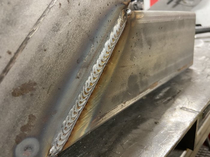 Välutförd svetssöm på metall med jämna svetspärlor och färgförändringar vid sömmen.