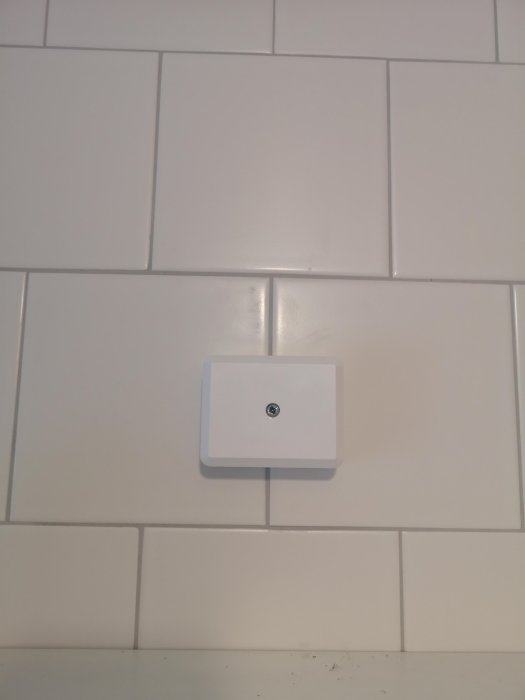 Vit kvadratisk eluttagskåpa på en vit kakelvägg ovanför ett badrumsskåp.