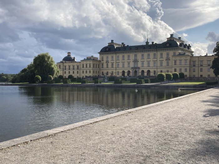 Ett storslaget slott vid vattnet med markerad arkitektur och en prydlig grön trädgård i förgrunden.