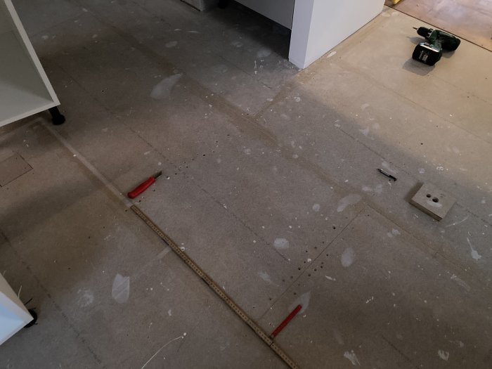 Delvis synligt nytt köksgolv av golvspånskiva med märkbart knarrande område, verktyg och mätinstrument syns.