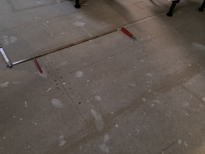 Bild på ett nylagt golvspånskiva med synliga skruvar och en mätsticka på ytan som visar arbete med golvinstallationen.