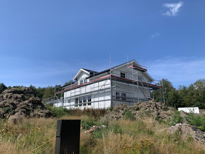 Ett hus under renovering med ställningar runtom och nymålade ytor mot en klarblå himmel.