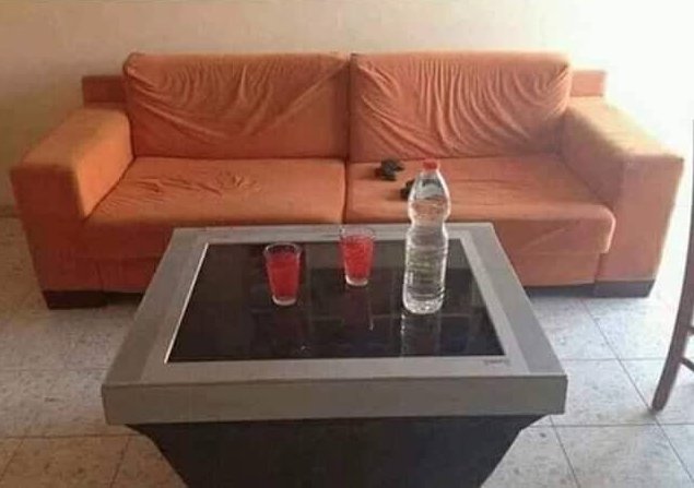 En beige soffa med två röda glas och en vattenflaska på ett glasbord.
