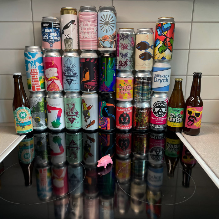 Samling av olika ölburkar och flaskor med konstnärliga etiketter på ett blankt köksbord.