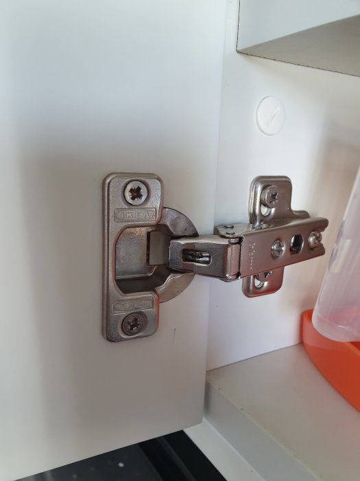 Gångjärn med Ikea/Blum-märkning på ett skåp, eventuellt från ett 90-talskök.