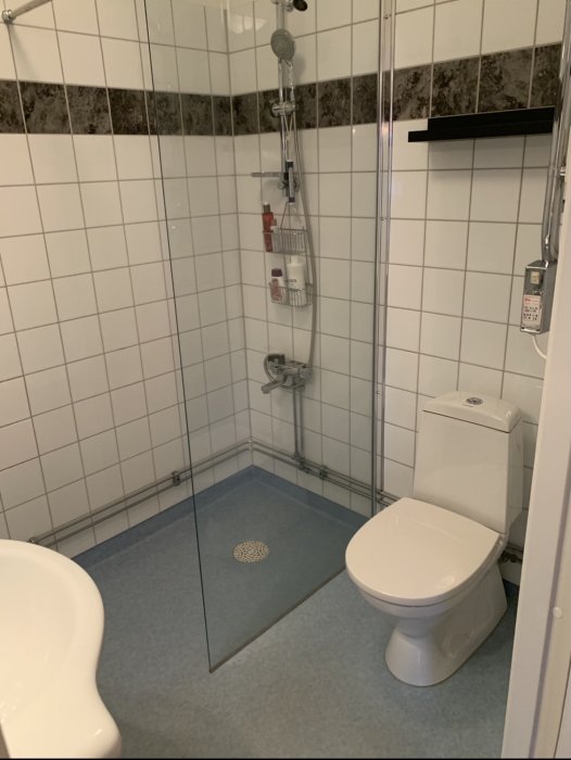 Renoverat badrum med nymålad blå golvfärg, vita väggar, duschhörna och toalett.