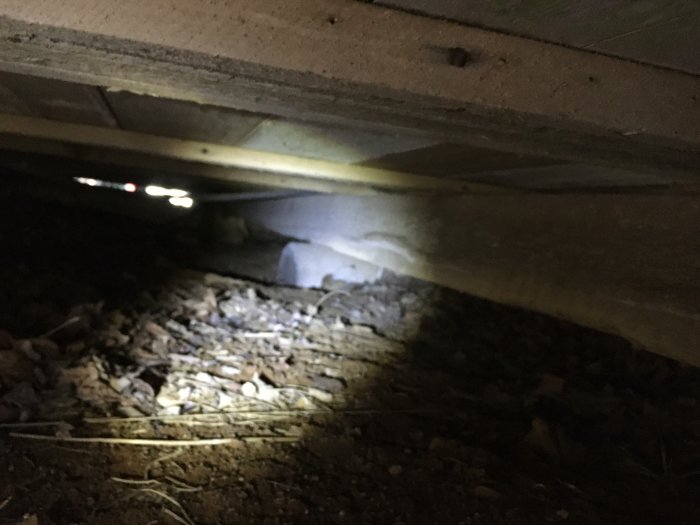 Underjordisk vy av bjälkar skarvade omlott över en stödplint, omgivna av stenar och grus.