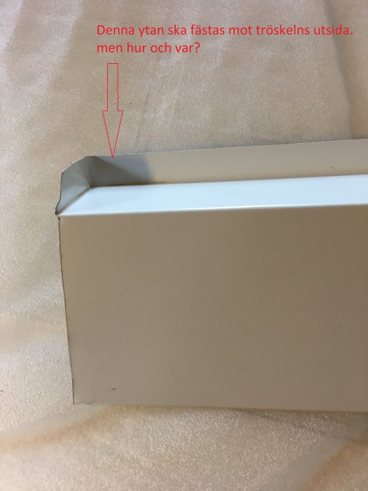 Närbild på ett tröskelbleck av aluminium med pil och text som beskriver monteringsfråga.