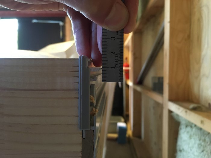 Hand som håller en linjal mot en del av en aluminiumtröskel som visar mått för montering av tröskelbleck.
