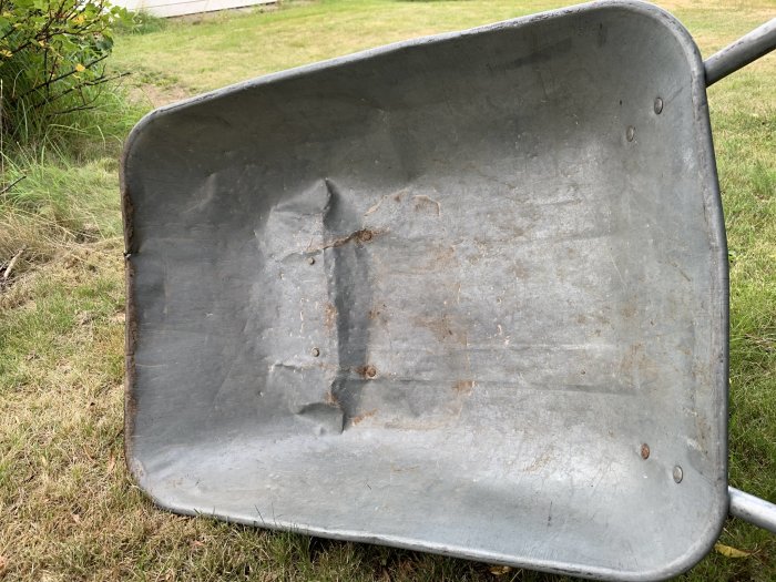 Sliten metallskottkärra på gräs, synbara tecken på mycket användning och rost.