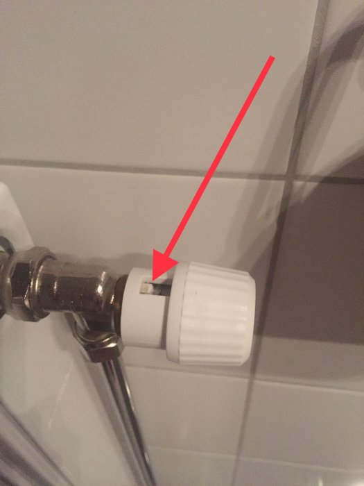 Radiator med vit termostat där markören för temperaturinställning saknas, röd pil visar var den satt.