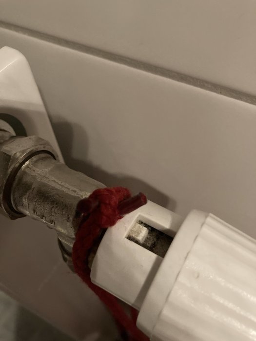 Närbild på en radiatorventil med saknad temperaturbricka där röd pil pekar och en liten handratt.