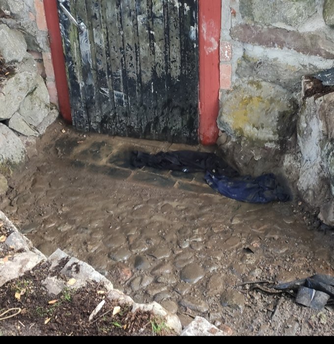 Vattenpölar framför en jordkällardörr med schifferplattor och omgivande stenmur.