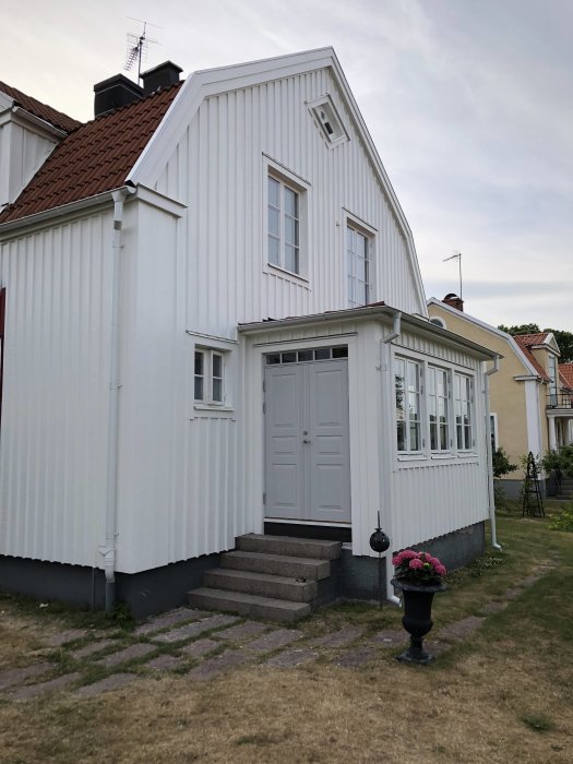 Gråa granitblocksteg från 1929 framför en vit trävilla, krysshamrade på toppen, med järnstolpe.