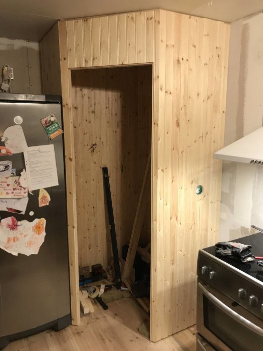 Under konstruktion hörnskafferi i kök med reglar, stenullsisolering och delvis installerad träpanel.