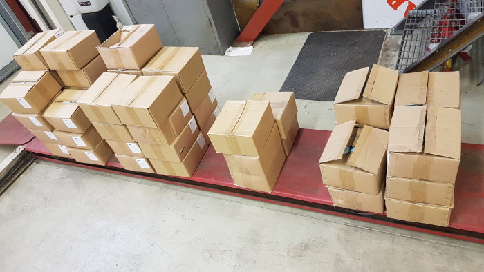 Staplar av bruna kartonglådor med skruvar till salu på ett lagergolv.