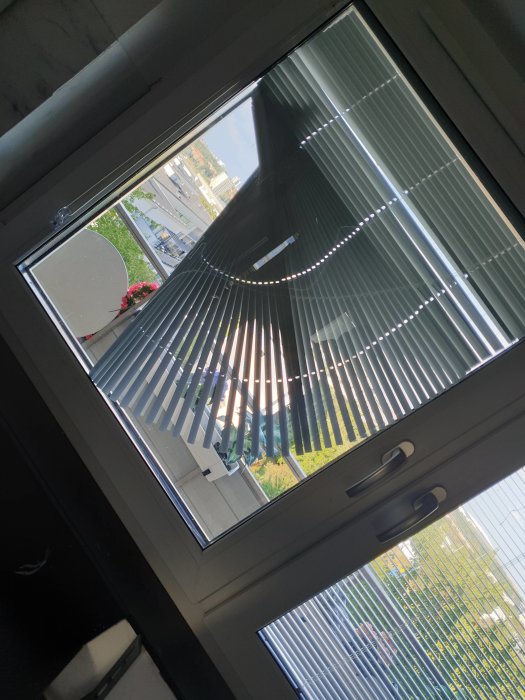 Fönster med mellanglas persienner, delvis sänkta, som skapar ett mönster av ljus och skugga.
