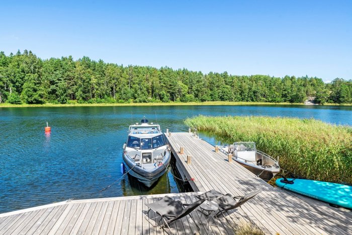 Motorbåt förtöjd vid en träbrygga, med en skog och en lugn insjö i bakgrunden.