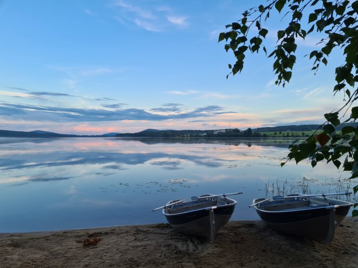 Kvällsvy över en spegelblank sjö i Järvsö med tre roddbåtar på stranden och ett färgglatt skymningshimmel.