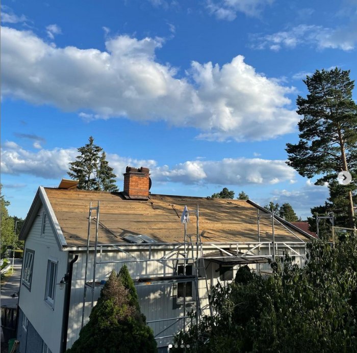 Renoverat hus med avlägsnat gammalt tegeltak och exponerad råspont, bostad i förgrunden och träd mot en himmel med moln.