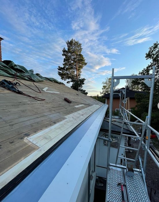 Takrenoveringsprocess med ny takfotsplåt och oskyddad råspont på ett husbygge.