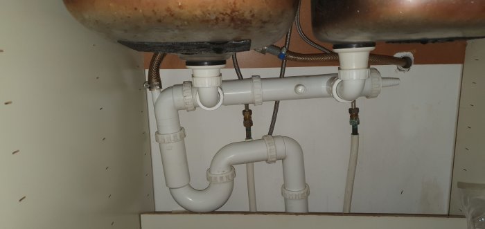 Rörinstallation under diskho med vattenlås och anslutningspunkter, redo för diskmaskinsanslutning.