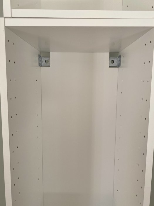 Metallfästen i överkant av vit bokhylla som stöd för hyllplan.