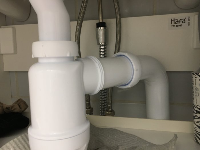 Vit VVS-installation under handfat med synliga rörkopplingar och flexibla anslutningar.