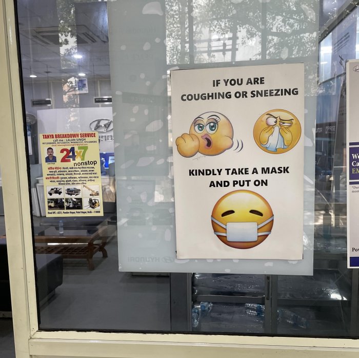 Affisch som uppmanar hostande eller nyssande personer att ta på sig en mask, visas med emojis.