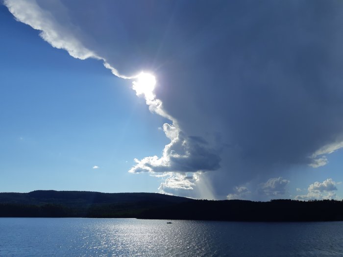 En stor mörk åskmoln närmar sig över en sjö med solen som bryter igenom molnen till vänster.