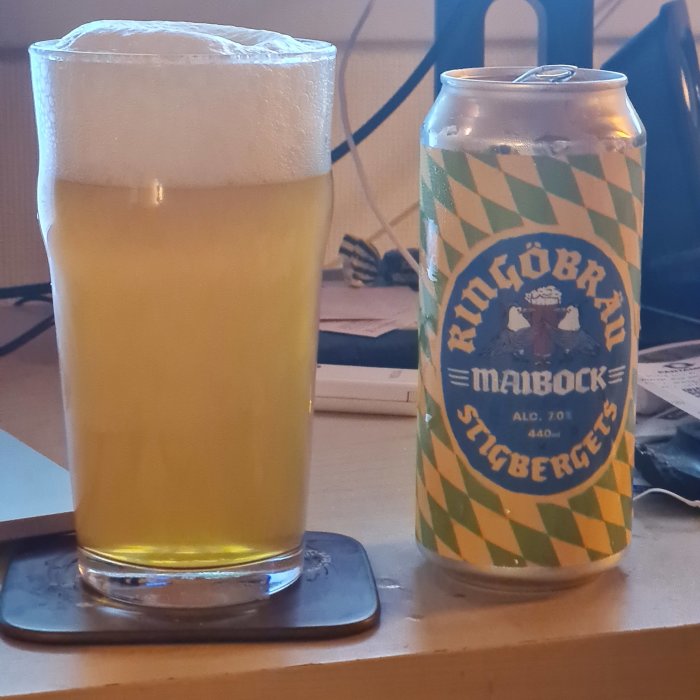 Ett glas grumlig Maibock-öl bredvid en burk från bryggeriet på ett bord.