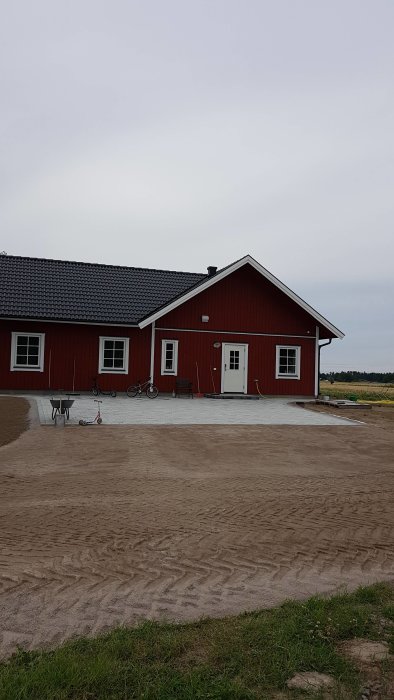 Röd villa med nylagt markstensområde framför, omgiven av grus och gräsmatta.