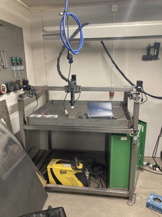 CNC-plasmaskärare i ett verkstadsutrymme med pågående kabeldragning och verktyg på väggen.