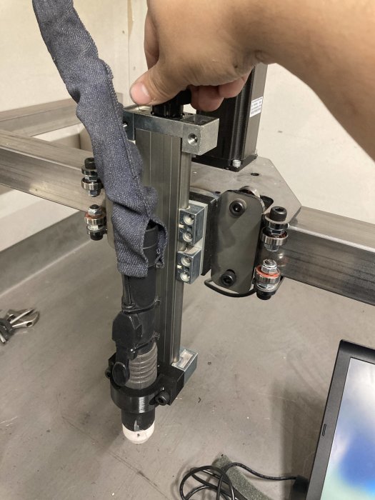 Hand justerar komponent på en CNC-plasmaskärare, med ofärdig kabeldragning och verktyg i bakgrunden.