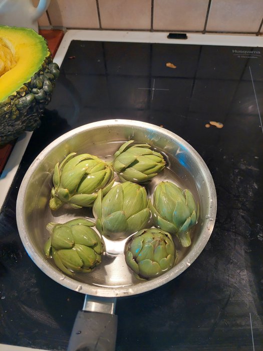 Flera färska kronärtskockor i en rostfri stålskål på ett köksbord.